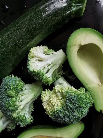 Raw broccoli, zucchini and half a pitted avocado on the black background. Only green vegetables. Healthy vegan eating. top view. high quality photoの写真素材