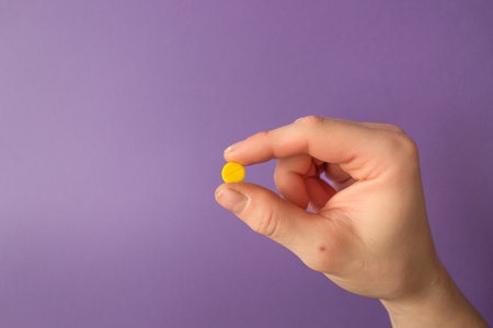 Man's hand holds a yellow round pill with his fingers. Very pericolor background. Daily dose of medication. . high quality photoの写真素材