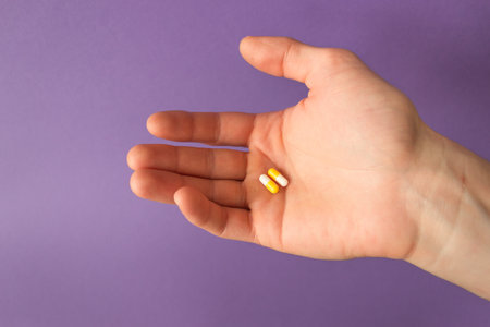 Man's palm holds two white-yellow capsules of vitamins. Very pericolor background. Daily dose of medication. high quality photoの写真素材