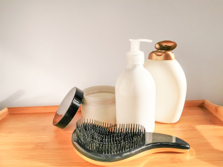 Hair care set: two white bottles of shampoo and conditioner, hair brush and open jar of hair mask with golden details on the wooden table. Horizontal composition and space for text.の写真素材