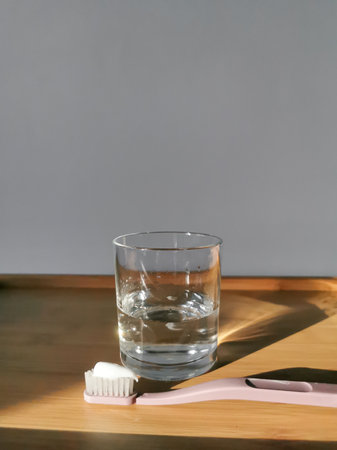Pink plastic toothbrush with paste and glass of water on the wooden table. For daily morning dental care. Space for text.の写真素材