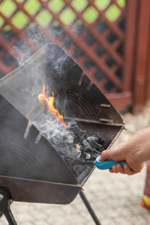 Male hand kindles fire in grill with long blue gas lighter. Man holding and using BBQ lighter to...
