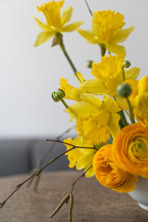 Arrangement with yellow ranunculus and narcissus flowers, birch twigs on japanese eco holder kenzan in vase. Ikebana of seasonal spring flowers, fresh bunch for interior. Easter holiday concept.の写真素材