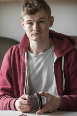 Sad young bankrupt showing his empty wallet and looking at camera. Upset man feeling stressed while looking at billfold.の写真素材