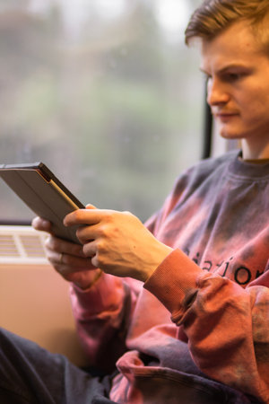 Smiling young man reading e-book when he traveling by train. Man sits at the train window and using...