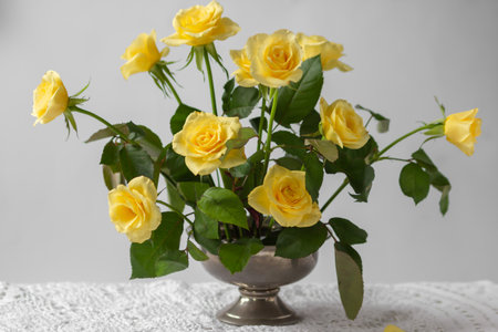 Floral arrangement of yellow garden rose flowers on pin frog in vintage vase. Spring ikebana decor on a lace tablecloth.の写真素材