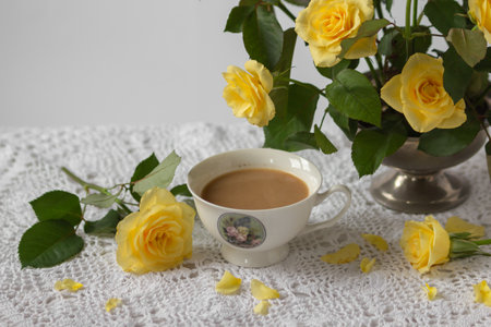 Still-life with porcelain cup of coffee, yellow garden rose flowers on pin frog in vintage vase on white lace tableclothの写真素材