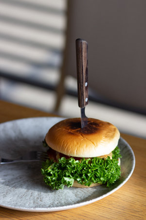 Big grilled vegan hamburger with green fresh salad on trendy gray plate, wooden table in cafe. Fast food concept.の写真素材