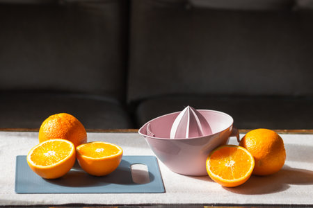 Manual plastic citrus juicer with a raw halved oranges on cutting board on the kitchen table. Healthy eating concept.の写真素材