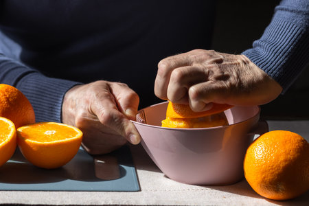 Senior man squeezing fresh orange juice with manual plastic juicer. Old man making homemade juice of halved oranges.の写真素材