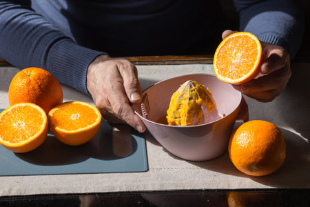 Senior man squeezing fresh orange juice with manual plastic juicer. Old man making homemade juice of halved oranges.の写真素材
