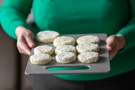 Old woman holding uncooked cottage cheese pancakes - syrniki on cutting board, ready to cook. Cooking healthy food.の写真素材
