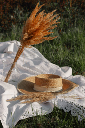 Retro straw hat with dry pampas grass on white sheet with weaving lace among green grass of spring meadow. Boho style.の写真素材