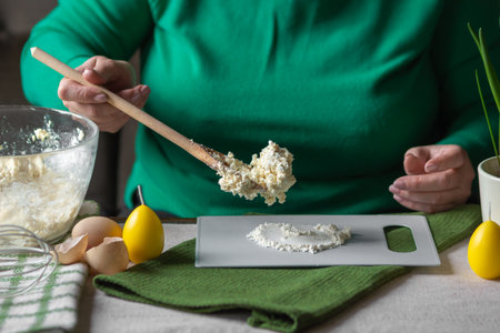 Senior woman adds spoonful of dough with cottage cheese to the flour on cutting board. Ingredients for cheese pancakes.の写真素材