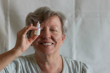 Happy senior woman holding in hand bottle of eyedrops in front of eye. Smiling female after using eyedrops. Eye health.の写真素材
