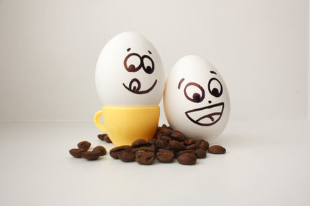 Egg with a face. Funny and cute to a coffee mug with coffee beans around. Useful and invigorating breakfast. Photo for your design. Joyful. Flirts showing the tongue. Cheerful company of two piecesの写真素材