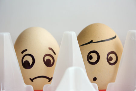 Eggs with painted face. The concept of hide and seek and shyness. Photo for your design. One egg in a cup of coffee and yellowの写真素材