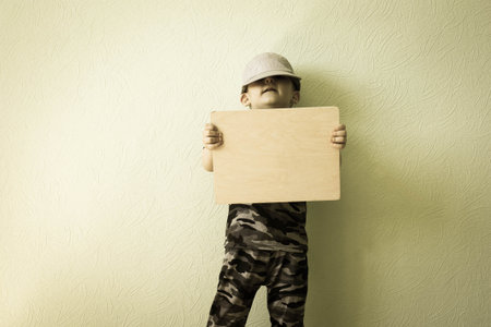 Concept of business. The child picked up a plaque at the wall in a gray cap and looked forward. Photo for your design. With a place under the text.の写真素材