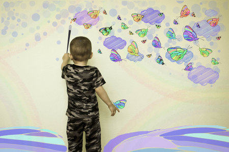 Concept of creativity child. The little boy draws on the wall. Butterflies and clouds. Photo illustration for your design.の写真素材