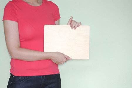 Sales and advertising concept. Place under inscription. Curly girl in red. Photo for your design. Holds a wooden sign. Place under the text is empty.の写真素材