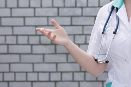 The doctor's concept. Girl in medical uniform with a stethoscope near a brick wall. With hand to side. Photo for your designの写真素材