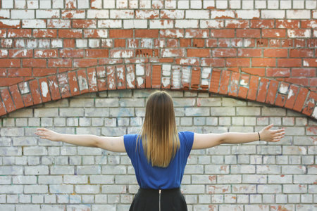 Female student concept. Beautiful girl near a brick wall. Keeps his hands spread out to the sides. Photo for your designの写真素材