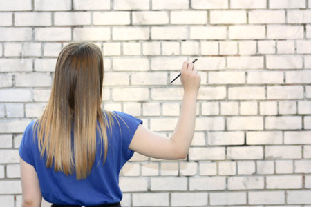 Female student concept. Beautiful girl near a brick wall. Write with a brush on the wall. Photo for your designの写真素材