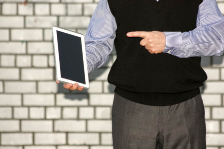 Business concept. A man is holding a tablet in his hand against a brick wall background and points at it with his finger. Photo for your design.の写真素材
