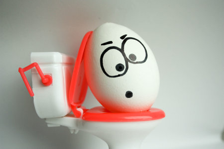 diarrhea is a comical concept. an egg with a painted face sitting on the toilet. photo for your design.の写真素材