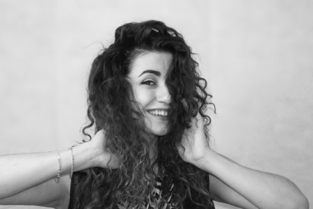 beautiful girl. curly-haired girl. photo for your design. black and white photography. monochrome. attractive girl with hands at face. playful girl. concept of happinessの写真素材