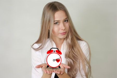 time concept. beautiful deushka is holding an alarm clock on a white background with a red heart. horizontal orientationの写真素材