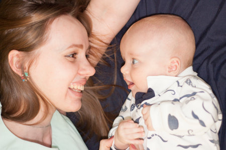 communication with the child. understanding. mom and baby. happiness maternity concept. mom and baby. Mom is smiling at the child. lie on a bed on a blue background.の写真素材