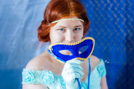 masquerade. portrait of a tender red-haired girl. in a blue historical dress. holds a mask in his handの写真素材