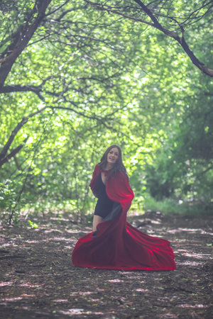 Witch in a red cloak among the forest halloween. escape attractive girl halloween magic and magic. ritual danceの写真素材