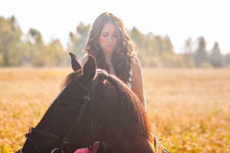 Doubting girl on a horse in a dress in the sun on the fieldの写真素材