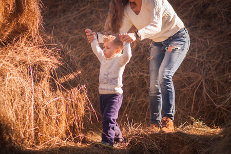 Mom and baby play together in the open air in the afternoon. games in nature. farm days. giant haystack and family on it. pediatric hyper activity and attention deficit disorder. sheet horizontal orientationの写真素材