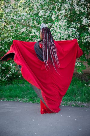Queen in the crown and royal mantle. Lovely girl on the background of a blooming garden. African American in redの写真素材