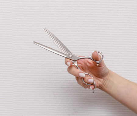 Close-up of female hand holding thinning grooming scissors with curved ergonomic design for pet fur care on plain surface.の写真素材