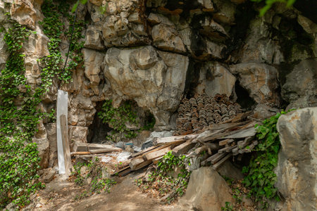 Scene shows shaded rocky nook with stacked red clay tiles, construction debris and green ivy growing over surrounding stone formationsの写真素材