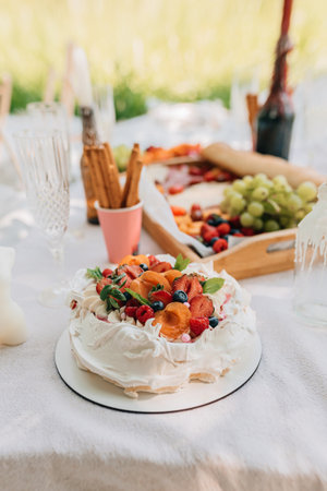 Outdoor pavlova cake with apricots and berries served during elegant summer picnic with fruit snacks and drinks.の写真素材