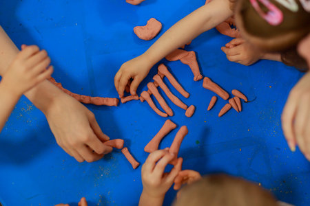 Children's hands modeling dinosaur bones from clay on blue table surface, collaborative educational...