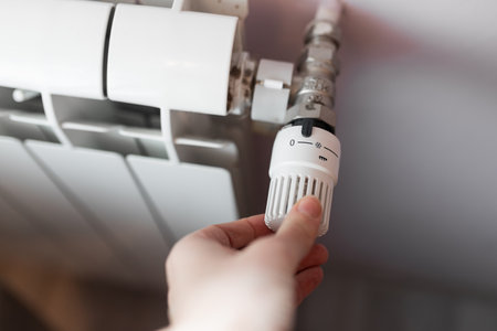 Closeup hand adjusting white plastic radiator thermostat knob set to zero with frost protection...