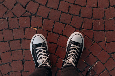 Two black high top sneakers with white laces on red patterned cobblestone street surface, showing...