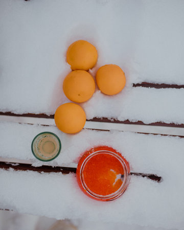 Flatlay composition of red jar, oranges, and shot glass on snow. Bright contrast between warm colors and cold surface creates winter festive mood.の写真素材