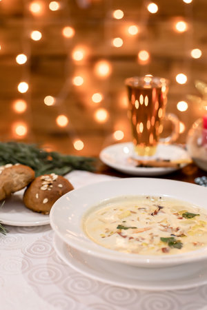 Bowl of hot creamy soup served with fresh parsley and bread rolls. Warm light and cozy Christmas decor in background create inviting restaurant atmosphere perfect for seasonal menuの写真素材