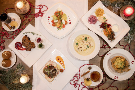 Top view of Christmas dinner table with assorted plates â meat, soup, salad, desserts and mulled wine among red decorations and candles.の写真素材