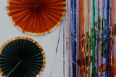 Large paper fans with metallic gold edges placed beside vertical rainbow foil strips forming vivid decorative backdrop suited for events, kids celebrations, party zones requiring bold visual accents.の写真素材