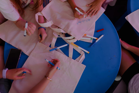 Child-friendly creative setup featuring canvas bags spread across blue tables, sketch pens scattered...