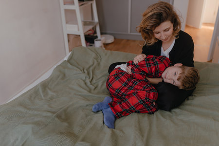 Soft warm tones show mother holding boy curled in her lap wearing red plaid pajamas, peaceful family...