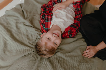 Soft bedroom scene showing child lying upside wearing red plaid pajamas, relaxed comfortable pose, playful indoor moment, warm home environment with natural light and casual lifestyle expression.の写真素材